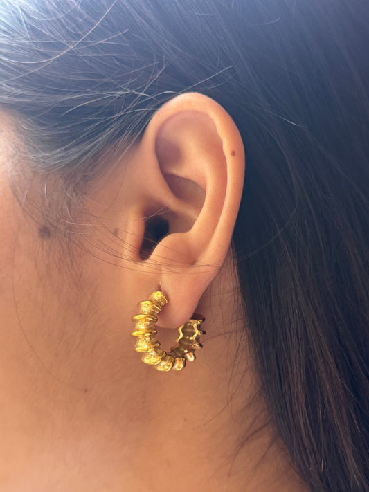 Gold hoop earring worn by a person with dark hair.
